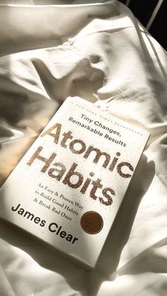 the book atomic habitts is laying on top of a bed with white linens