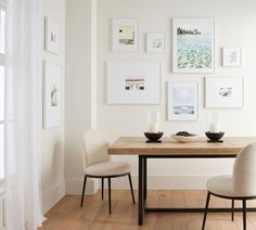 a dining room table with two chairs and pictures on the wall above it in white