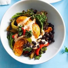 a white bowl filled with black beans, broccoli and other vegetables on top of a blue table