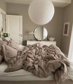 an unmade bed in a bedroom next to a large mirror and white cabinetry