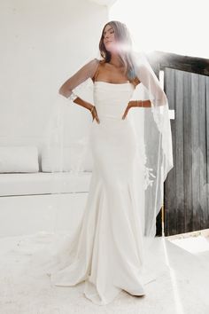 a woman in a white wedding dress posing with her veil over her head and looking off to the side