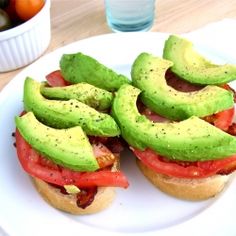 two sandwiches with avocado and tomatoes on a white plate