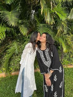 two women standing next to each other in front of palm trees and grass with one kissing the other