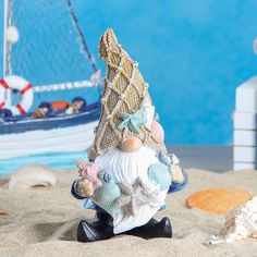 a gnome figurine sitting in the sand next to a sailboat and seashells