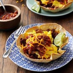 two plates with taco shells on them, one filled with chili and the other topped with cheese