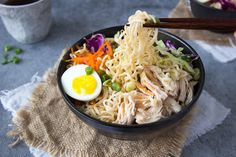 a bowl filled with noodles, meat and veggies next to chopsticks