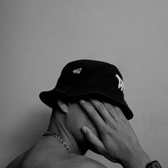 a shirtless man covers his face with his hands while wearing a new york yankees hat