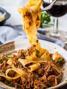 a fork is lifting up some pasta from a bowl with meat and sauce on it