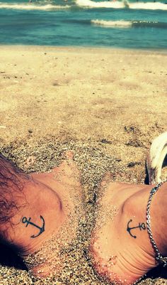 two feet in the sand with anchor tattoos on them