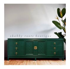 the sideboard is painted green and has brass hardware on it, along with a potted plant