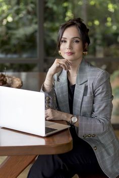 a woman sitting at a table with a laptop in front of her and looking off to the side