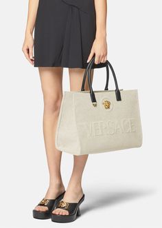 Crafted from canvas, this tote bag is adorned with a central La Medusa plaque and tonal debossed Versace logo lettering. The contrasting top handles are crafted from leather, and the spacious interior has two zipped pockets and a protector strap. Versace Bag, Versace Logo, Womens Designer Bags, Large Tote Bag, Leather Items, Canvas Tote Bag, Large Tote, Designer Bags, Clutch Handbag