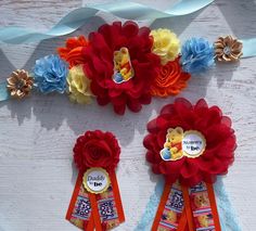 three red and yellow ribbons with winnie the pooh badges on them next to flowers