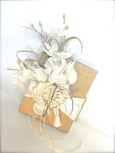 a bouquet of white flowers sitting on top of a brown box with gold ribbon around it