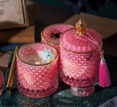 three pink glass jars with tassels on a table