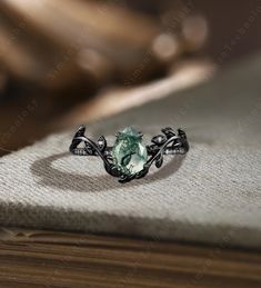 a ring with an oval green stone in the center on top of a table next to a book