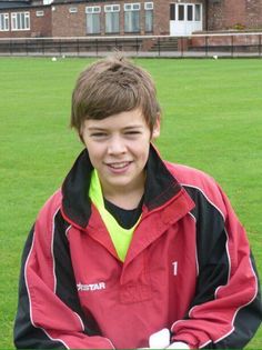 a young boy in a red and black jacket standing on top of a green field