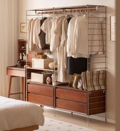 an organized closet with clothes hanging on rails and shoes in the bottom drawer, next to a bed