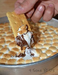 a person is dipping some ice cream on top of a waffle crust cake with chocolate and marshmallows