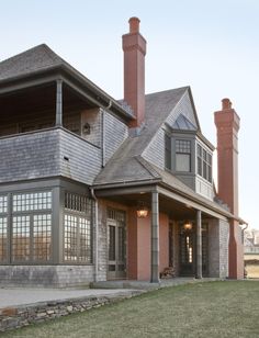 a large gray house sitting on top of a lush green field next to a tall red brick building