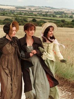 three women walking down a dirt road in long dresses and hats, one wearing a hat