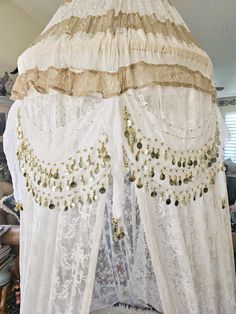 a canopy bed covered in white lace and gold sequins with curtains over it