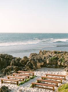 wooden benches sitting on top of a sandy beach next to the ocean