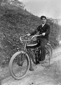 an old black and white photo of a man on a motorcycle riding down a dirt road