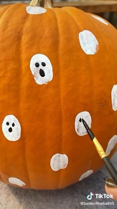 someone is painting a pumpkin with white polka dots on it and there are holes in the pumpkin