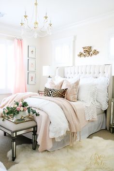 a white bed topped with lots of pillows next to a pink curtain and window sill