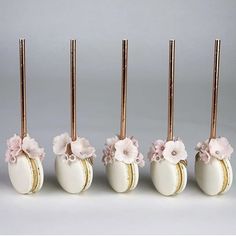 four white vases with pink flowers and gold sticks sticking out of them, all lined up in a row