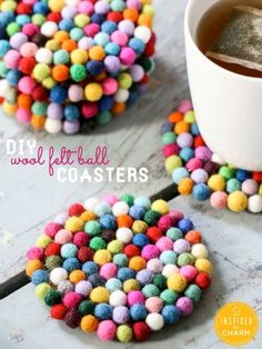 colorful felt ball coasters are sitting on a table next to a cup of coffee