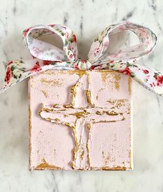 a cross is wrapped in pink and gold ribbon on a white marble surface with red flowers