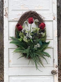 a wreath with red flowers and greenery hangs on the side of a white door