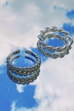 two silver rings sitting on top of a blue and white cloud filled sky with clouds in the background