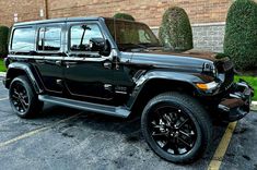 a black jeep parked in a parking lot next to a brick wall and shrubbery