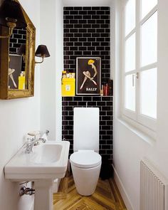 a white toilet sitting next to a bathroom sink under a mirror on a wall above a wooden floor