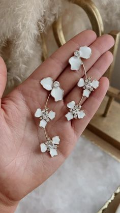 the white flower earrings are being held in someone's hand, while they have been placed