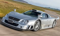 a silver sports car driving down a road next to an open field with grass and hills in the background