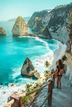 two women are walking up some stairs to the beach with blue water and cliffs in the background