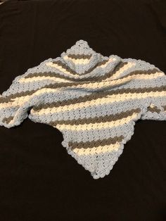 a crocheted baby blanket laying on top of a black tablecloth covered in white and gray stripes