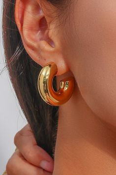 A woman wearing chunky gold hoop earrings. Gold Hoop Earrings Thick, Gold Thick Hoops Earrings, Modern Chunky Hoop Earrings, Modern Chunky Metal Earrings, Chunky Metal Hoop Earrings Modern Style, Minimalist Chunky Hoop Earrings, Thick Golden Hoop Earrings, Modern Chunky Metal Hoop Earrings, Simple Jewellery