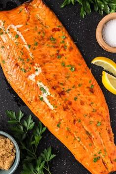 a large piece of fish sitting on top of a table next to some lemons and parsley