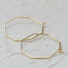 two gold hexagonal hoop earrings on a white surface