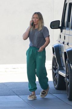 a woman is talking on her cell phone while walking down the street in green sweatpants