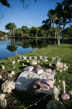 a picnic on the grass with flowers and candles in front of a lake surrounded by palm trees