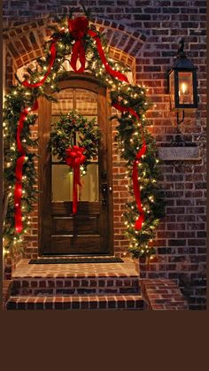 a christmas wreath on the front door of a brick house with lights and garlands around it