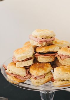 a pile of biscuits with ham and cheese on them sitting on a glass platter