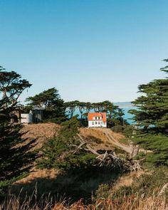 a white house on top of a hill with trees around it and the ocean in the background