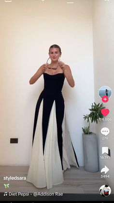 a woman in a black and white dress standing next to a plant